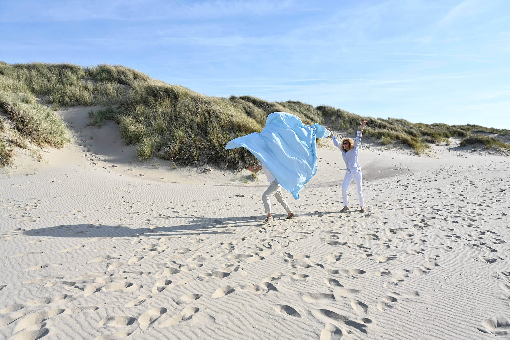 2 Girls on a photoshoot running after a blue backdrop on a windy beach in Zeeland, the Netherlands